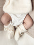 Baby's legs in white knitted booties and a bodysuit, resting on a soft textured blanket.