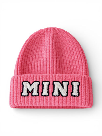 Pink knitted beanie with the word "MINI" embroidered in black and white on the front.