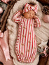 Newborn girl in a striped candy cane outfit with a matching bow, sleeping on a cozy blanket.