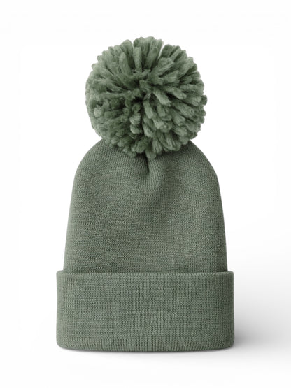 Green knit beanie with a fluffy pom-pom on top, set against a white background.