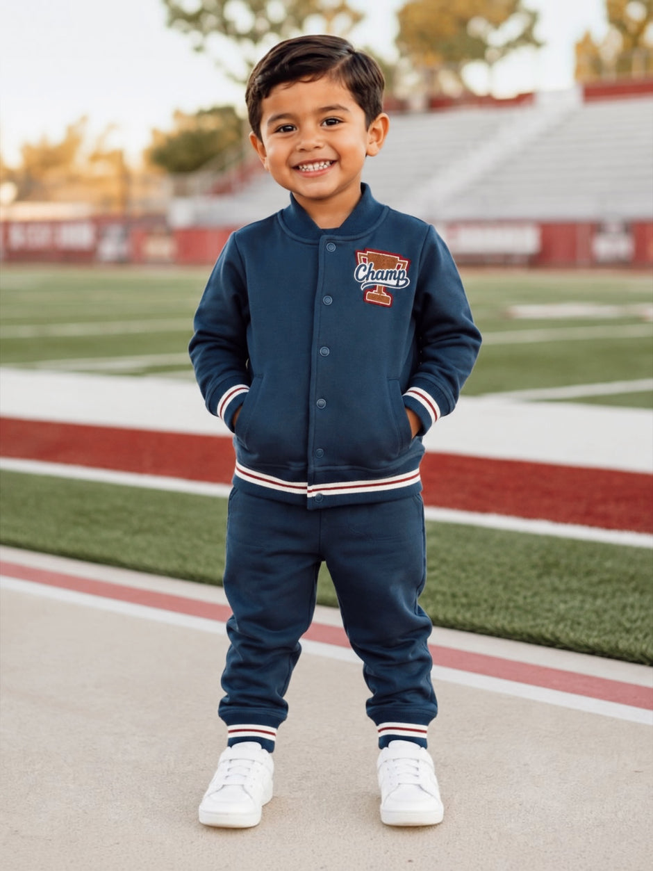 Smiling child in a navy tracksuit stands on a sports field, showcasing a "Champ" logo and white sneakers.
