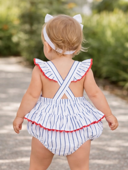 Child in a striped swimsuit with red trim, wearing a headband, walking on a path surrounded by greenery.