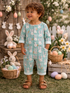 Smiling child in a bunny-print outfit, surrounded by Easter decorations, flowers, and pastel eggs.