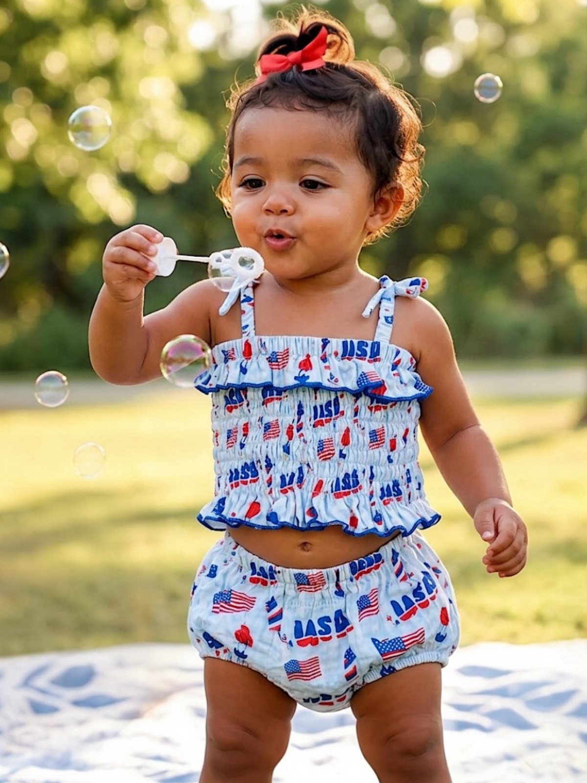 Toddler playing with bubbles outdoors, wearing a patriotic-themed swimsuit, smiling in a sunlit garden.