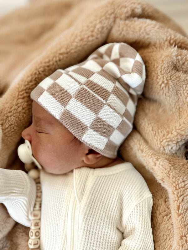 Baby wearing a checkered beanie, peacefully resting on a soft blanket.