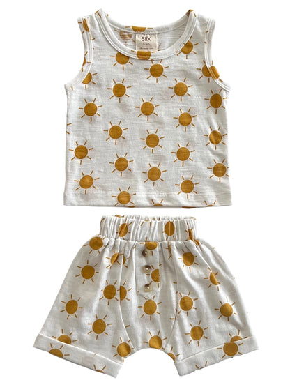 White children’s outfit featuring a tank top and shorts, both decorated with yellow sun patterns.