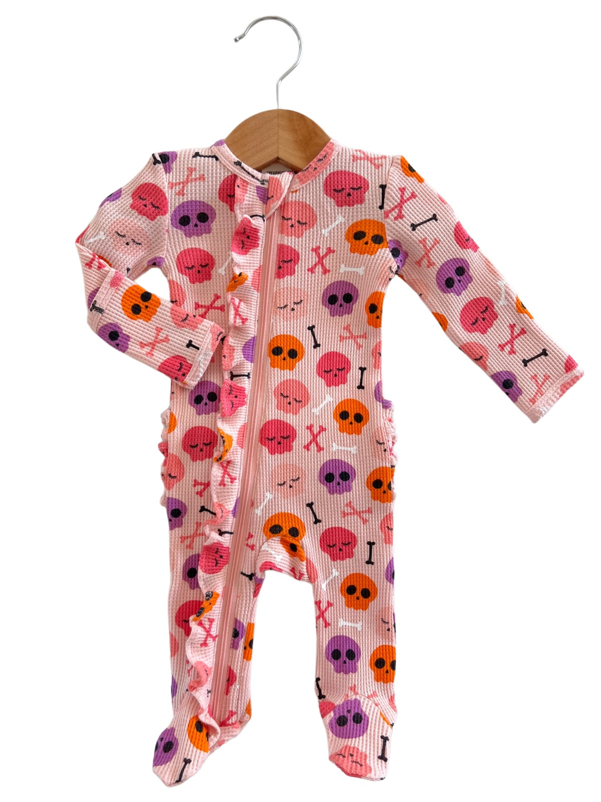 Pink children's pajamas with skull and crossbones pattern, hanging on a wooden hanger.