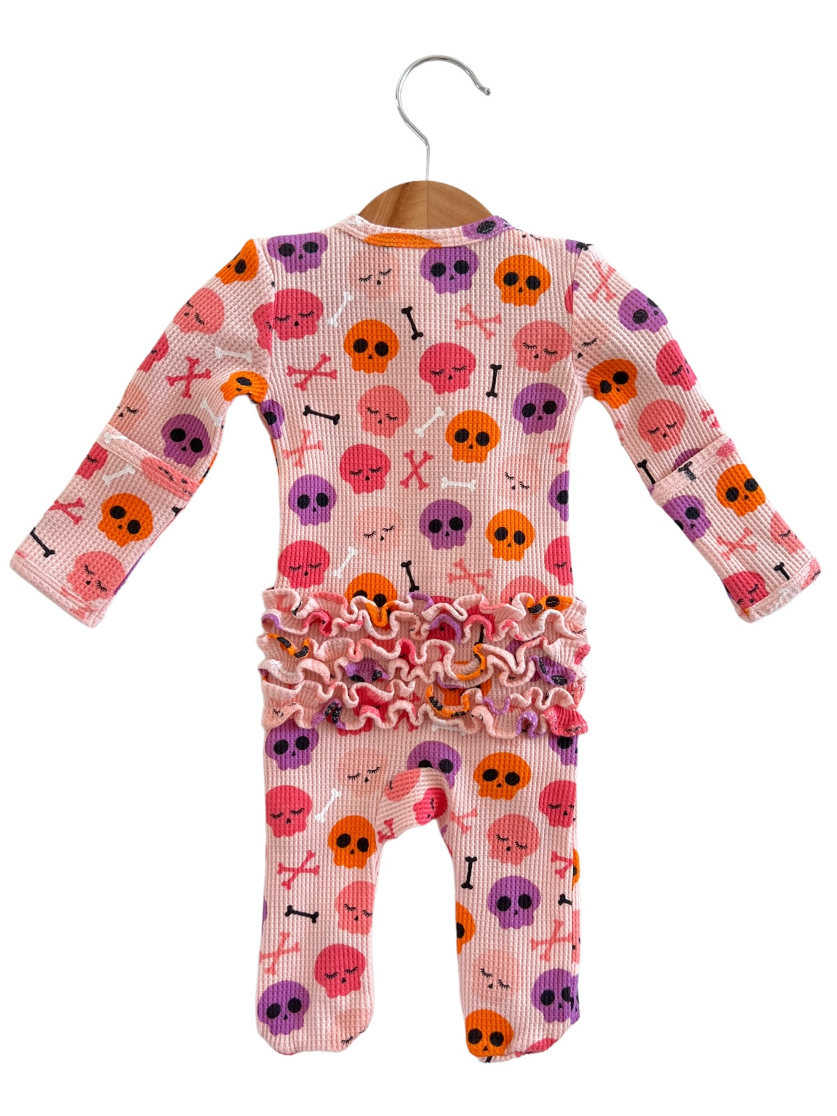 Pink baby onesie with skull and crossbones pattern, accented with ruffled trim at the waist.