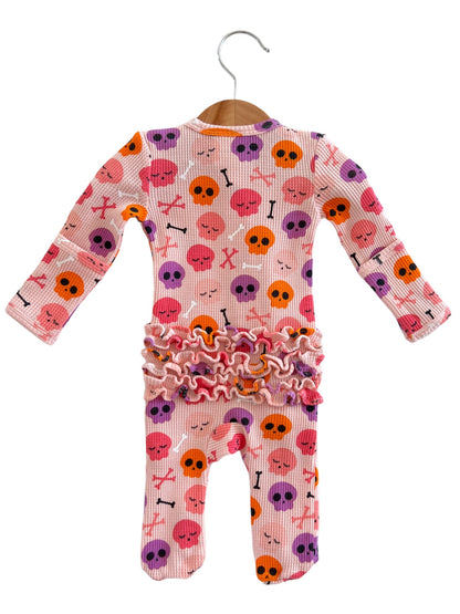 Pink baby onesie with skull and crossbones pattern, accented with ruffled trim at the waist.