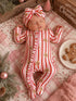 Baby girl sleeping in a festive striped onesie with gingerbread men, wearing a matching headband, surrounded by holiday decor.