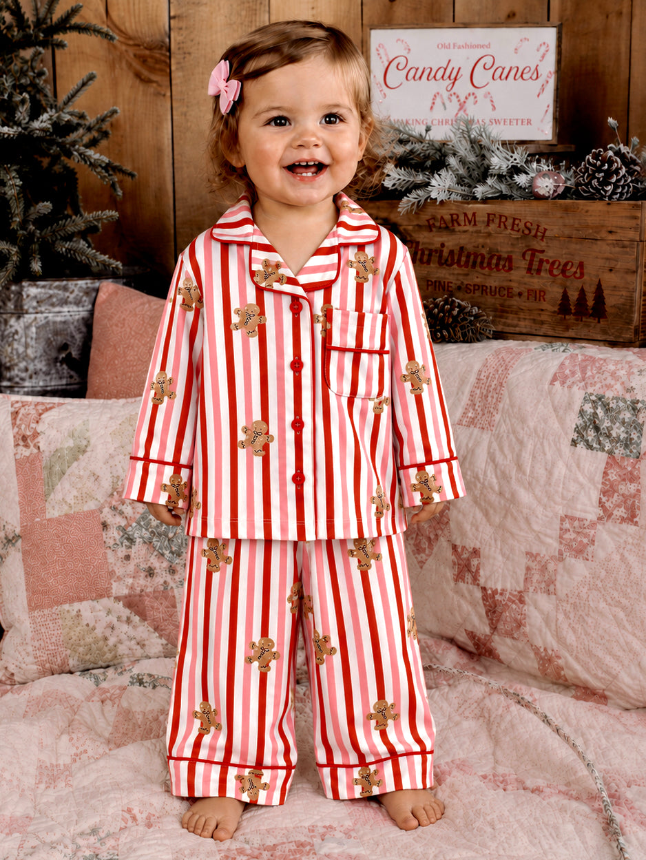 Smiling child in red and white striped pajamas with gingerbread, standing on a quilted bed.