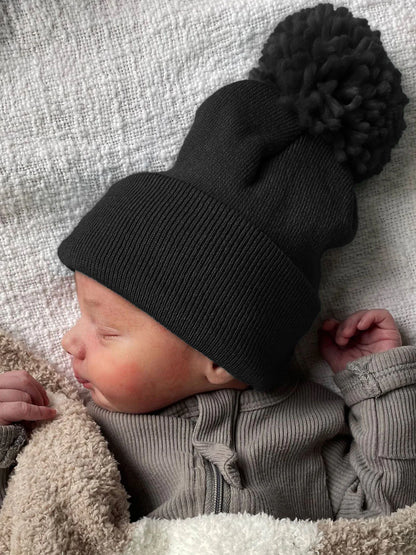 A peaceful newborn in a dark beanie, wrapped in a soft blanket, sleeping on a textured surface.
