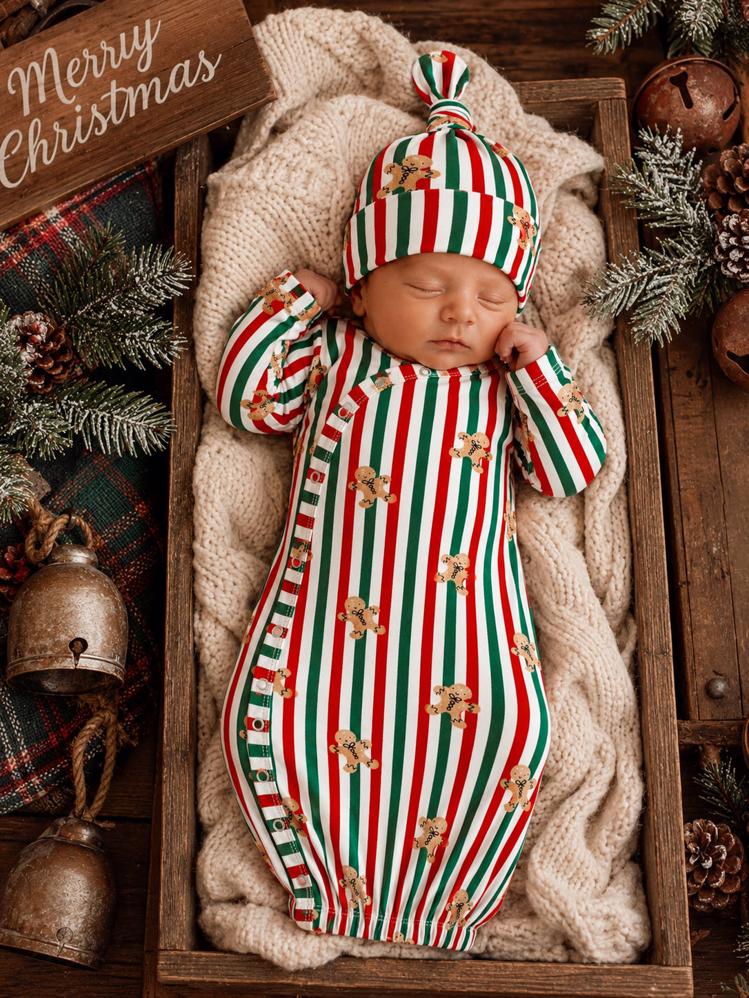 Sleeping baby in festive striped pajamas with gingerbread designs, nestled in a cozy blanket in a wooden crate.