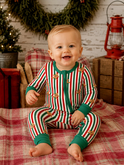 Smiling baby in festive striped pajamas, sitting on a blanket with holiday decor in the background.