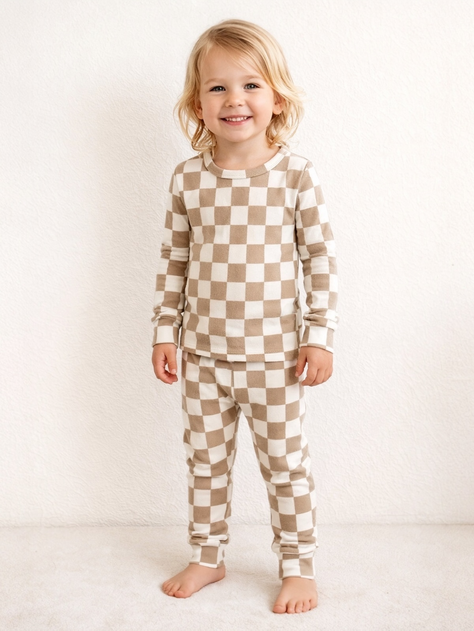 Smiling child in checkered pajamas stands on soft white surface against a textured white wall.
