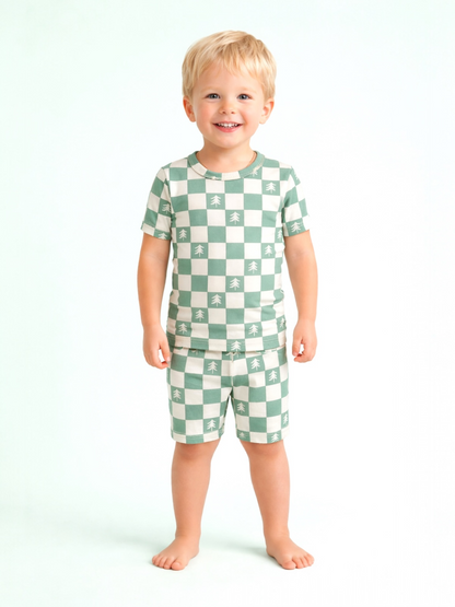 Smiling child in green and white checkered pajamas with tree patterns, standing barefoot against a light background.