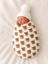 Newborn swaddled in a bear-patterned blanket, wearing a white hat, resting peacefully on a soft background.