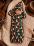 Sleeping baby in a green plaid outfit with puppy prints, resting on a cozy blanket with rustic decor around.