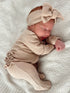 Sleeping baby in a beige outfit and headband, resting on a soft, textured blanket.