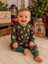 Smiling baby in festive pajamas with a dog pattern, sitting in a cozy holiday setting with Christmas decor.