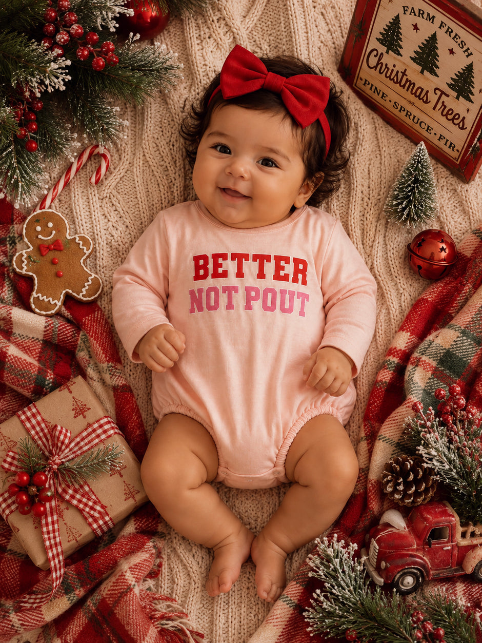Smiling baby in a pink onesie with "Better Not Pout" text, surrounded by festive holiday decorations.