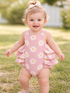 Smiling baby in a pink floral swimsuit, playing in a grassy area with a sunny background.