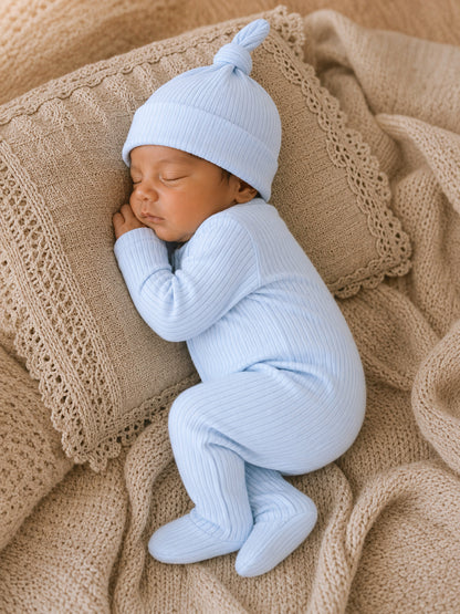 Sleepy newborn in a light blue outfit and hat, nestled on a cozy cream-colored blanket.