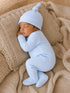 Sleepy newborn in a light blue outfit and hat, nestled on a cozy cream-colored blanket.