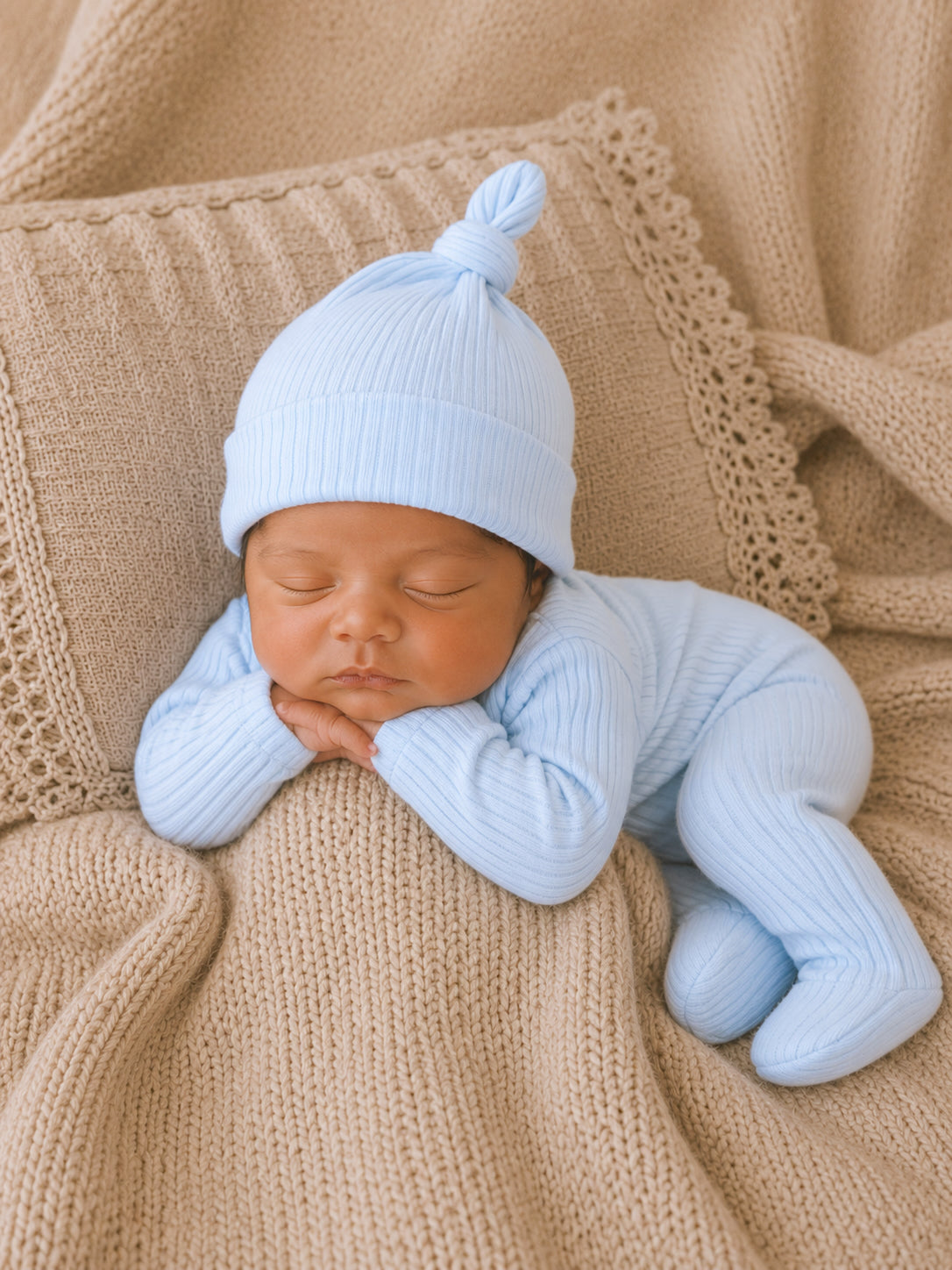 Newborn sleeping peacefully in a soft blue outfit on a cozy beige blanket.