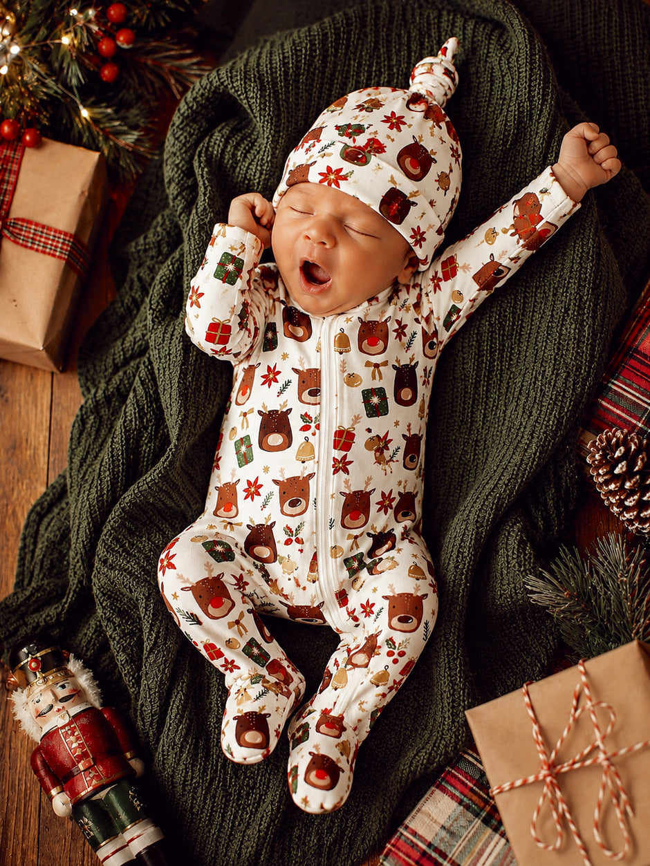 Adorable baby yawning in festive animal print pajamas on a cozy blanket, surrounded by holiday decorations.