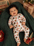 Smiling baby in festive onesie surrounded by Christmas decor, sitting on a green blanket with a toy truck.