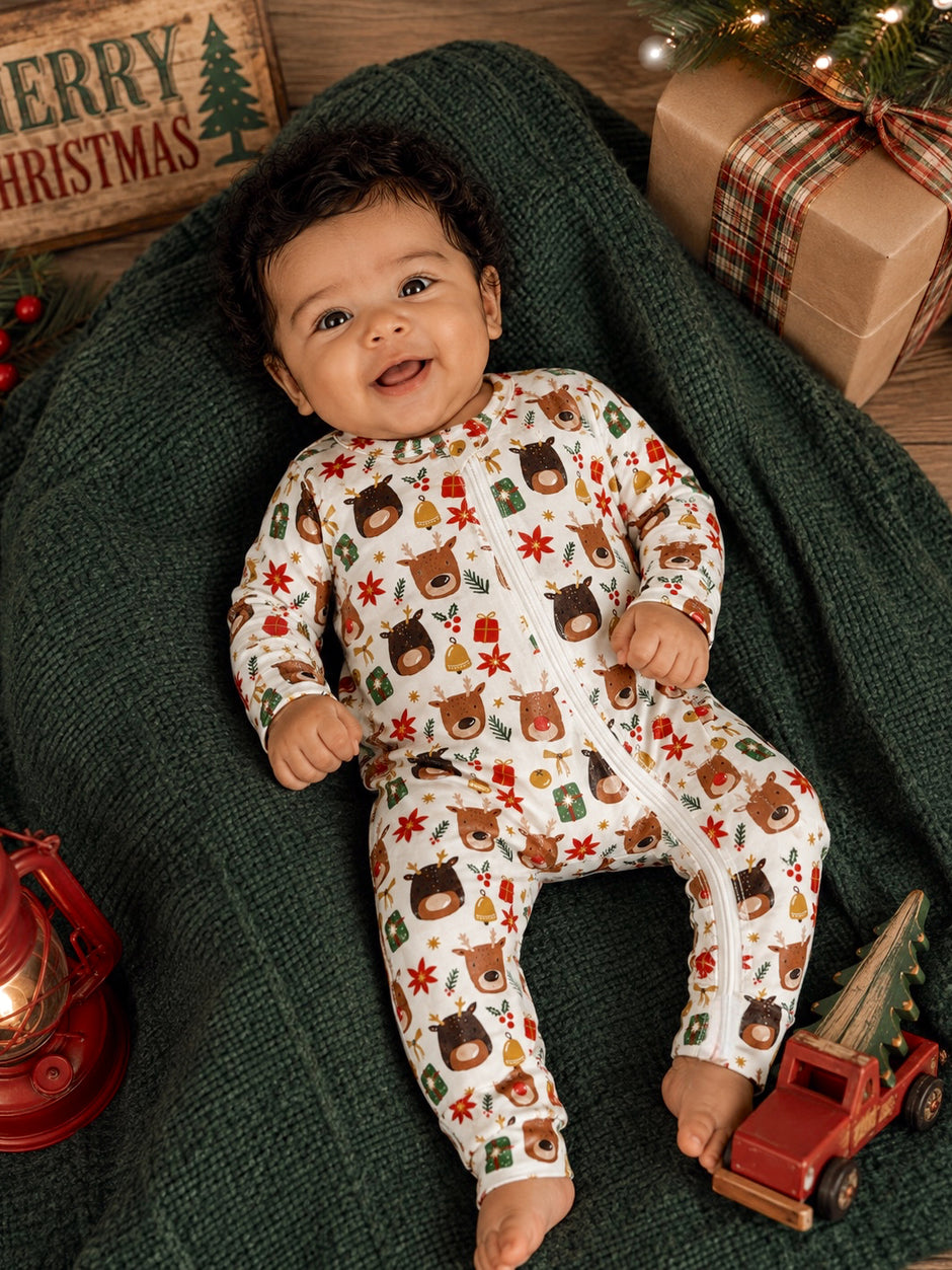 Smiling baby in festive onesie surrounded by Christmas decor, sitting on a green blanket with a toy truck.