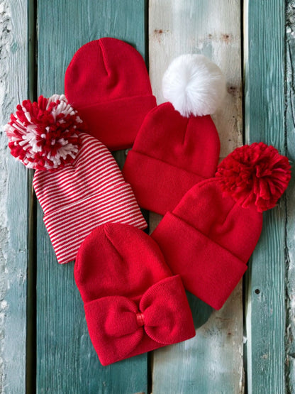 Collection of red winter hats, featuring different styles and pom-poms, on a rustic wooden background.