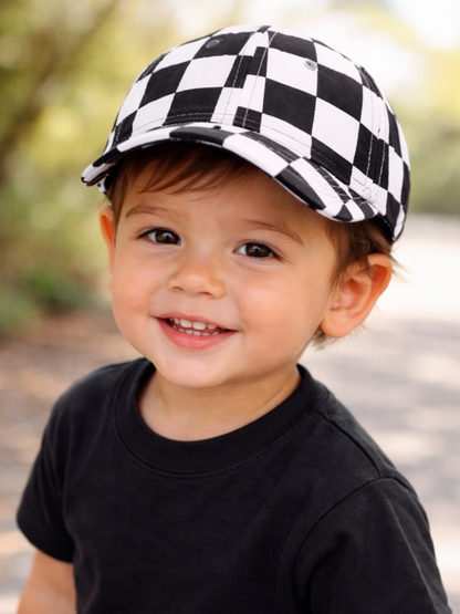 Smiling young boy wearing a black shirt and a black and white checkered cap outdoors.