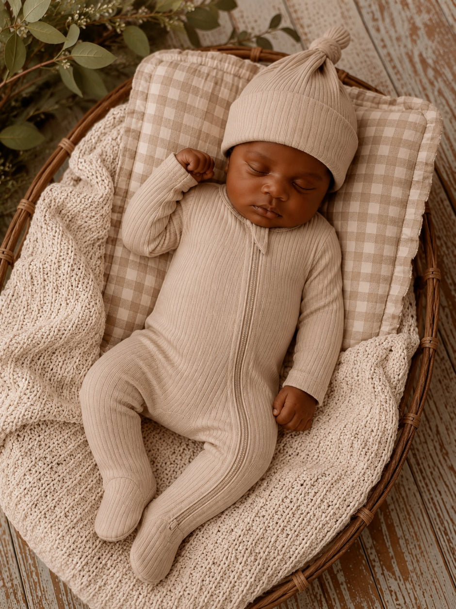 Infant peacefully sleeping in a cozy basket, wearing a beige outfit and matching hat, surrounded by soft textures.