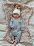 Infant in striped onesie and white hat, lying on a pink knitted blanket.