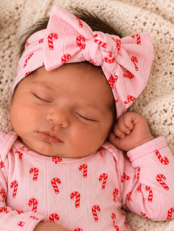 Sleeping baby girl wearing a candy-cane patterned outfit and a large pink bow on a knit blanket.