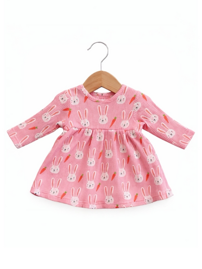 Pink dress with bunny and carrot pattern, hanging on a wooden hanger. Perfect for kids' spring fashion.