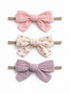 Three hair bows in pink, floral, and lavender fabric, each attached to a hair elastic.