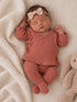 Sleeping baby in a cozy rust outfit with a bow, resting beside a soft stuffed bunny on a textured blanket.