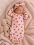 Newborn girl sleeping in pink bear-patterned gown with a matching headband, alongside a plush bunny toy.