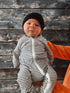 Infant in a striped onesie and black beanie held against a wooden background.