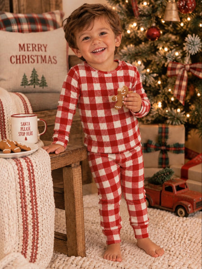 Smiling child in red and white pajamas holds a gingerbread cookie by a Christmas tree and festive decorations.