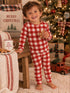 Smiling child in red and white pajamas holds a gingerbread cookie by a Christmas tree and festive decorations.