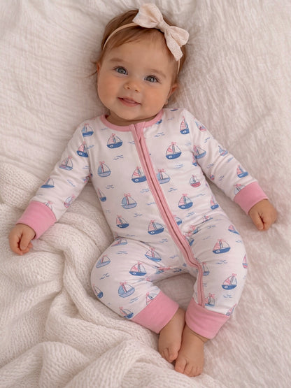 Baby in a sailboat-patterned onesie smiles while sitting on a cozy blanket. A bow adorns her hair.
