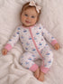 Baby in a sailboat-patterned onesie smiles while sitting on a cozy blanket. A bow adorns her hair.