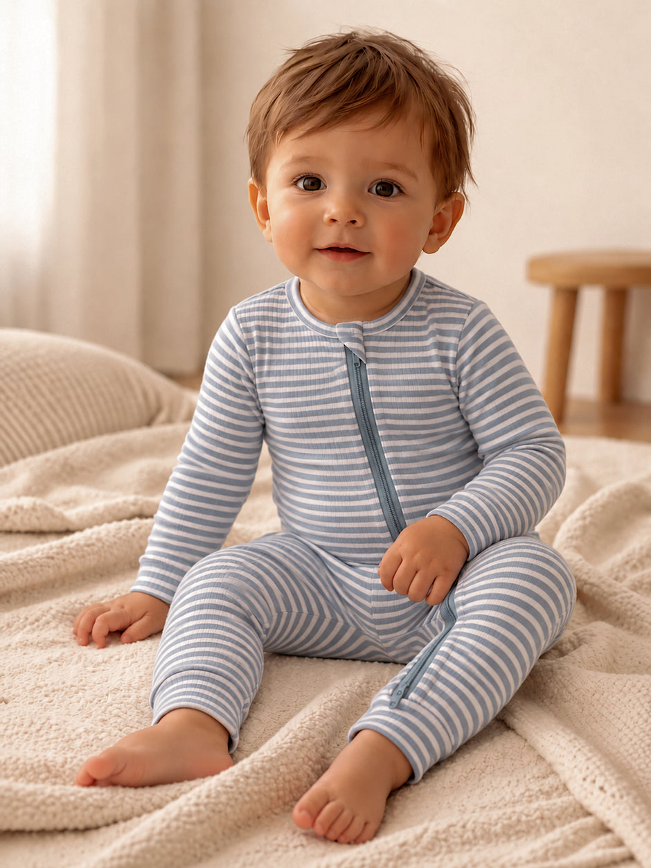 Smiling toddler in a striped blue pajama set, sitting on a cozy blanket in a bright room.