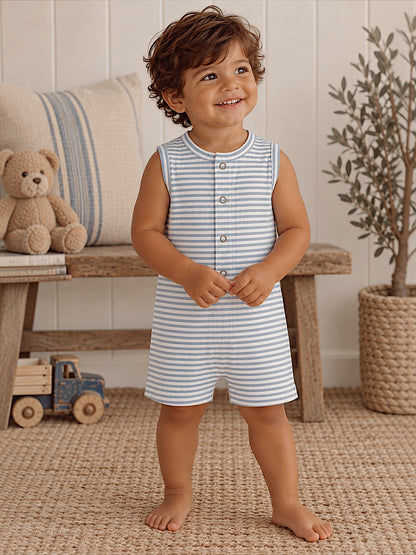 Smiling toddler in striped outfit stands on a woven rug, next to a toy truck and a teddy bear.