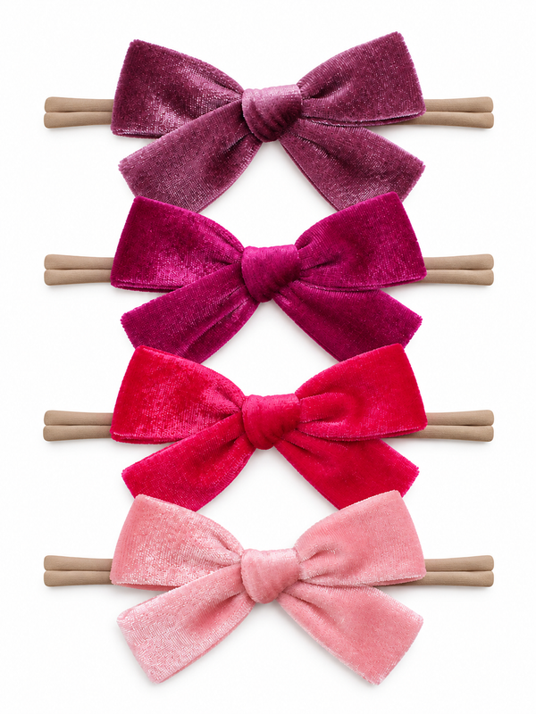 Four velvet hair bows in varying shades of pink, arranged on hair ties against a light background.