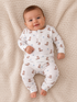 Smiling baby in cozy pajamas with boot and star patterns, lying on a soft blanket.
